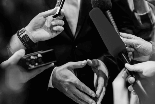 multiple hands holding microphones recording a politician